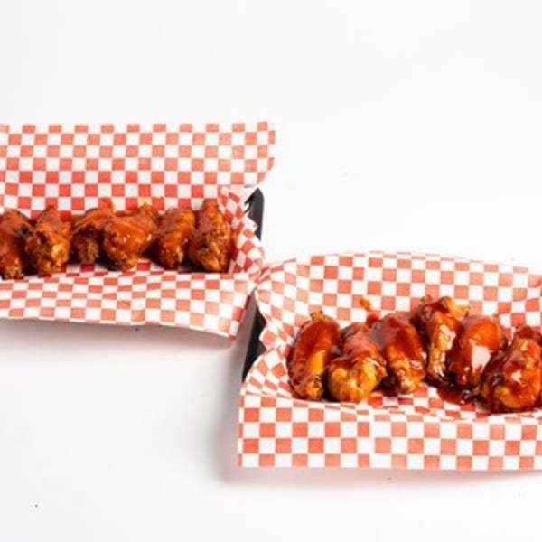 Two servings of saucy chicken wings in red and white checkered paper trays.