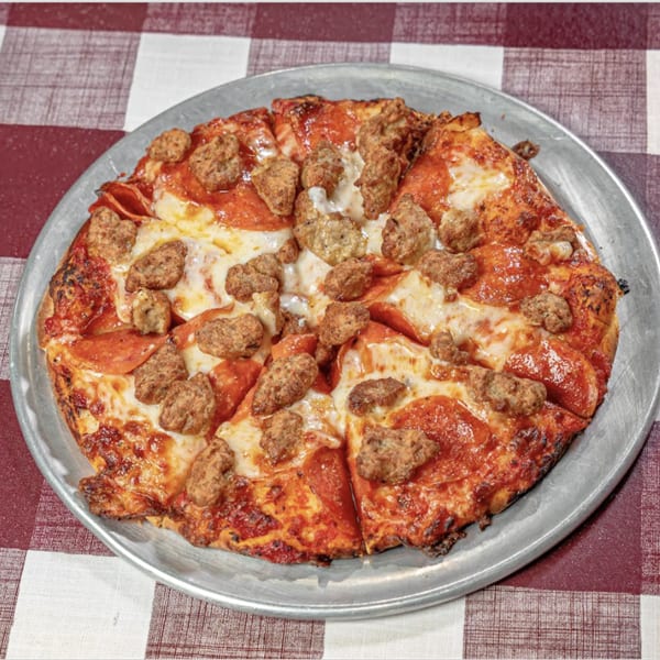 A pepperoni and sausage pizza on a metal pan, resting on a red and white checkered tablecloth.