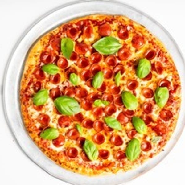 A whole pepperoni pizza topped with fresh basil leaves on a clear plate.
