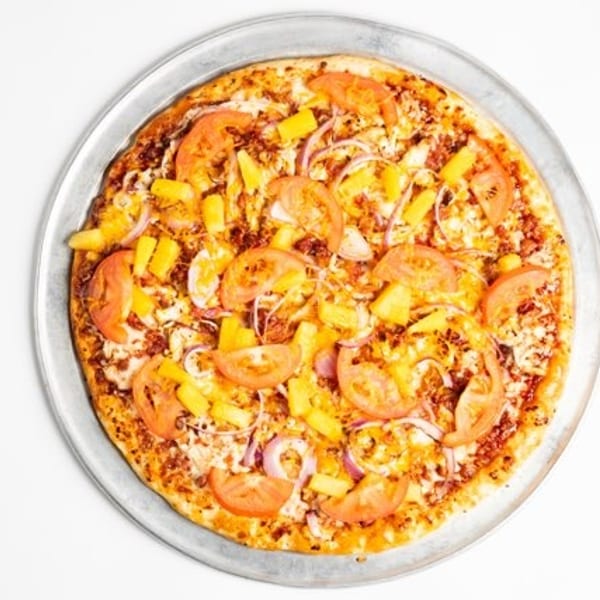 A whole pizza with pineapple, tomatoes, and red onions on a metal pan.