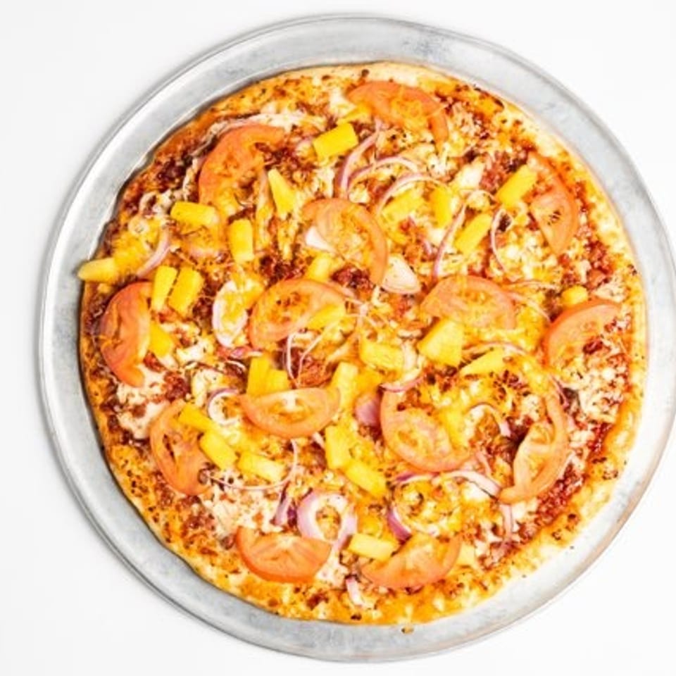 A whole pizza with pineapple, tomatoes, and red onions on a metal pan.