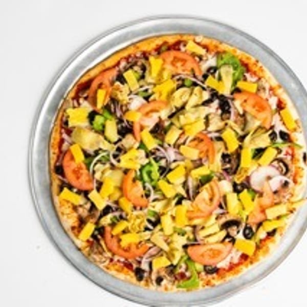 Whole pizza with pineapple, tomatoes, olives, and artichoke hearts on a metal pan.