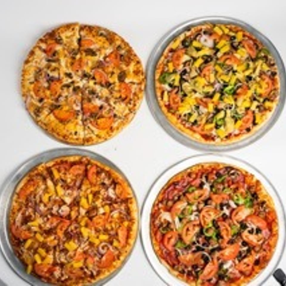 Four pizzas with various toppings, including vegetables and meats, on a white surface.