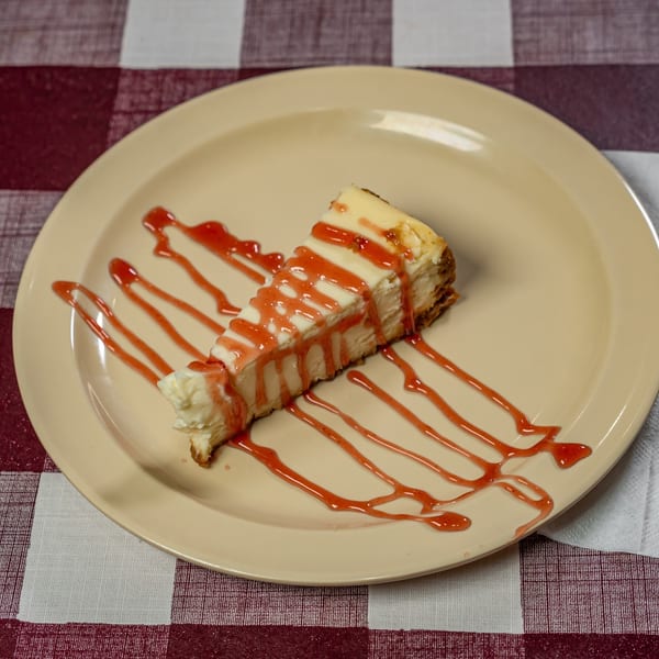 A slice of cheesecake drizzled with strawberry sauce on a beige plate with a white fork.